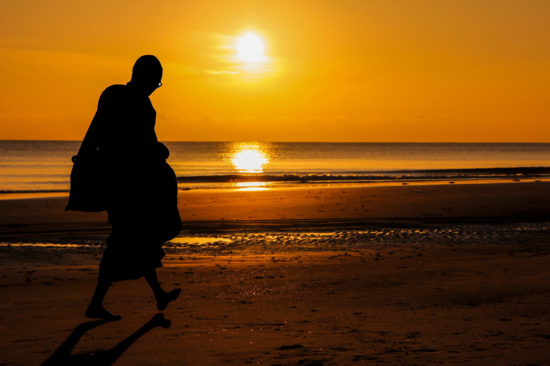 Monk silhouette at sunset on beach